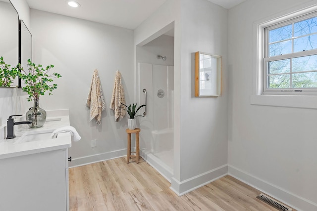 bathroom with baseboards, walk in shower, wood finished floors, and a sink