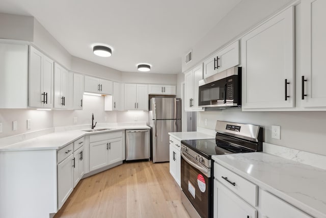 kitchen featuring white cabinets, stainless steel appliances, a sink, light wood-style floors, and light stone countertops