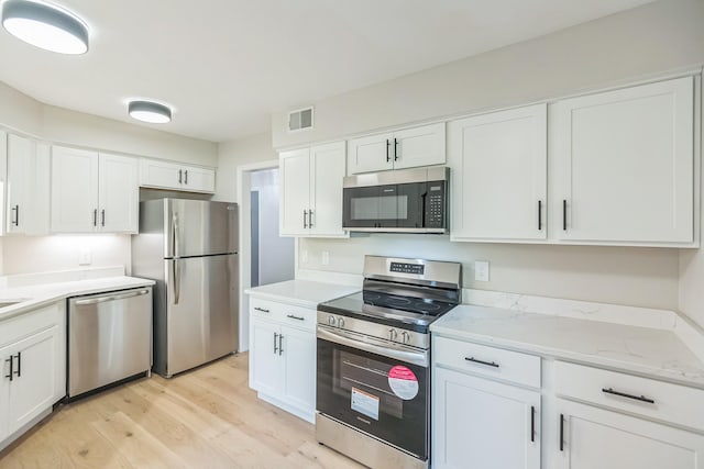 kitchen with appliances with stainless steel finishes, light wood finished floors, white cabinetry, light stone countertops, and visible vents
