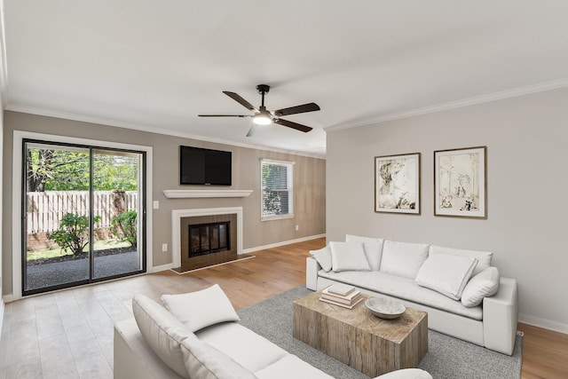 living area featuring ceiling fan, baseboards, ornamental molding, and light wood-style flooring