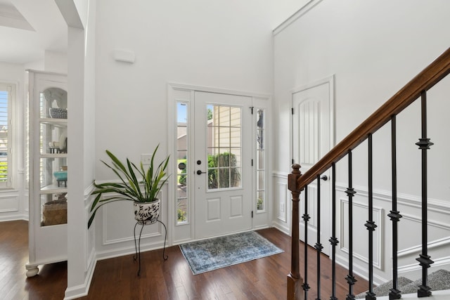 entryway featuring dark wood-style floors, a decorative wall, and stairs