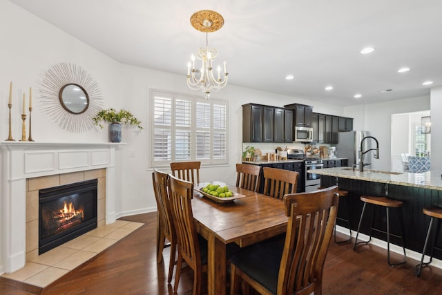dining area with wood finished floors, recessed lighting, a chandelier, a tiled fireplace, and baseboards