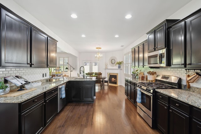 kitchen featuring stainless steel appliances, a sink, a peninsula, a chandelier, and light stone counters