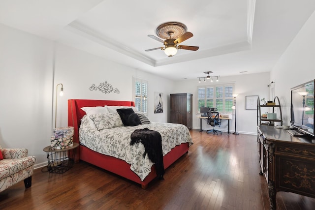 bedroom featuring a tray ceiling, an office area, wood-type flooring, baseboards, and crown molding