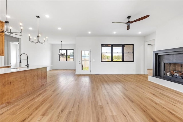 unfurnished living room with recessed lighting, a fireplace with raised hearth, a sink, light wood-type flooring, and ceiling fan with notable chandelier