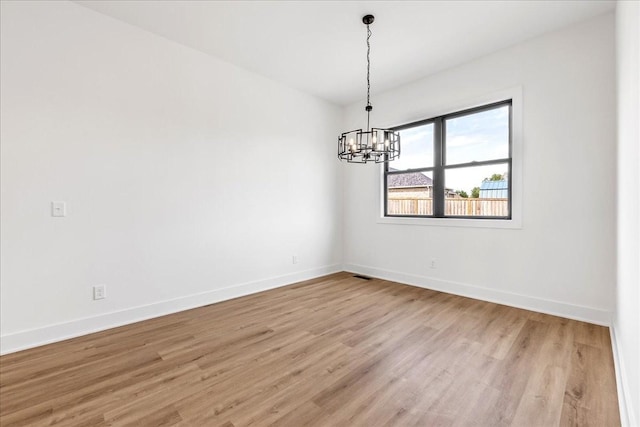 spare room featuring a chandelier, visible vents, light wood finished floors, and baseboards