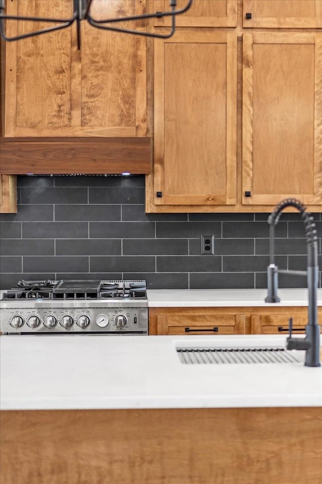 kitchen with stainless steel gas stovetop, light countertops, a sink, decorative backsplash, and brown cabinetry