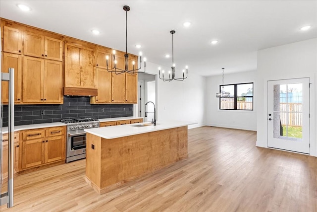 kitchen featuring a sink, a chandelier, light wood finished floors, backsplash, and high end stainless steel range oven