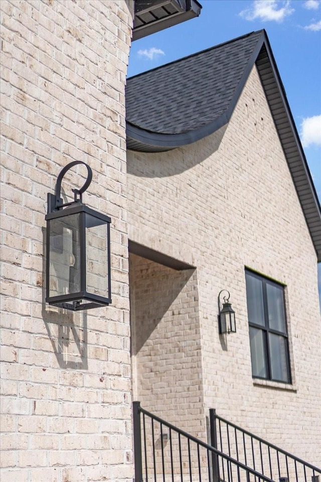 exterior space featuring brick siding and roof with shingles
