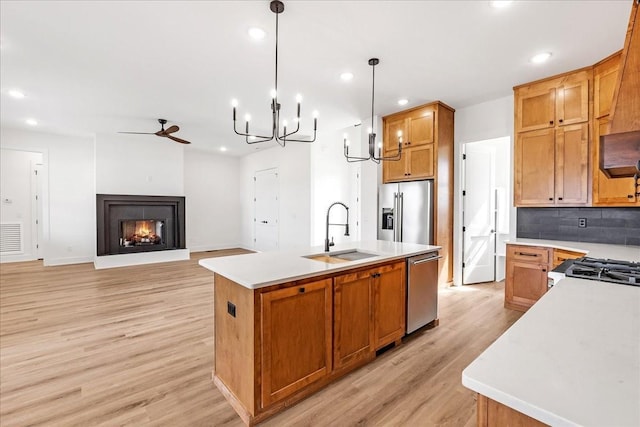 kitchen featuring light wood finished floors, stainless steel appliances, a sink, recessed lighting, and an island with sink