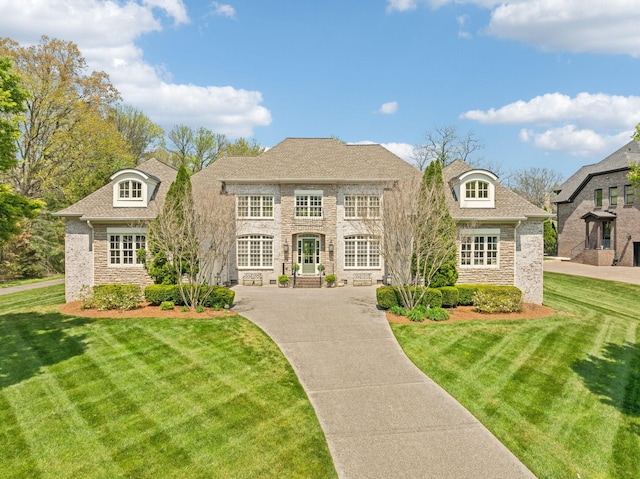 french country home with stone siding, a front lawn, concrete driveway, and a shingled roof