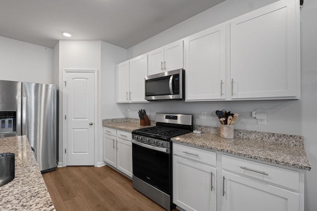 kitchen with wood finished floors, white cabinetry, appliances with stainless steel finishes, light stone countertops, and recessed lighting