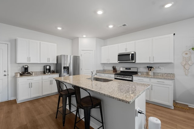 kitchen featuring stainless steel appliances, a sink, visible vents, a breakfast bar, and an island with sink