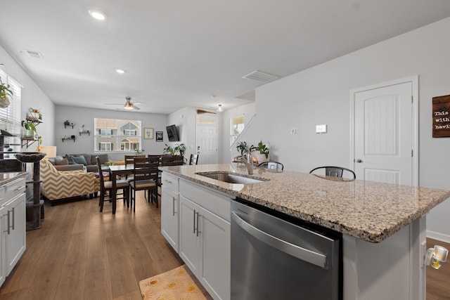 kitchen featuring an island with sink, dishwasher, wood finished floors, a sink, and ceiling fan