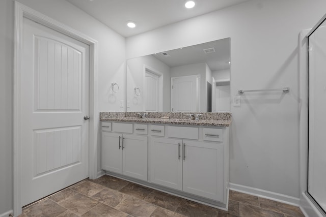 full bath with stone finish floor, double vanity, an enclosed shower, a sink, and baseboards