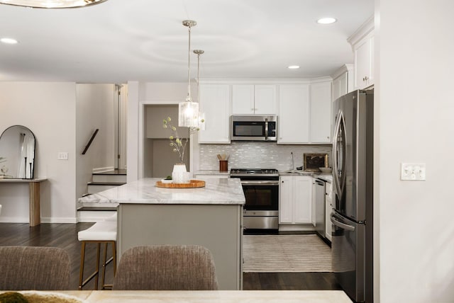 kitchen with light stone counters, white cabinets, stainless steel appliances, dark wood finished floors, and a kitchen island