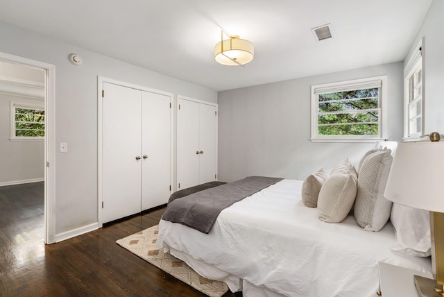 bedroom with dark wood finished floors, baseboards, multiple closets, and visible vents