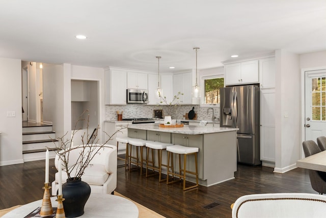 kitchen with white cabinets, stainless steel appliances, a center island, a kitchen breakfast bar, and backsplash