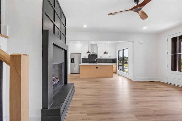 living room featuring recessed lighting, a fireplace with raised hearth, light wood-type flooring, baseboards, and ceiling fan