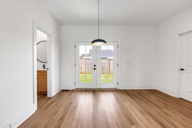 unfurnished dining area with light wood-type flooring, french doors, and baseboards