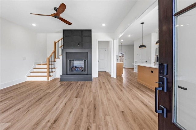 unfurnished living room with stairway, light wood finished floors, a ceiling fan, baseboards, and a fireplace