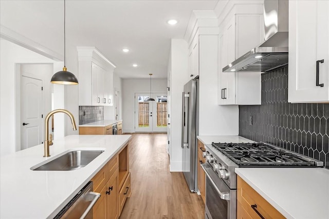 kitchen featuring backsplash, wall chimney range hood, a sink, light wood-style floors, and high quality appliances
