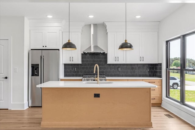 kitchen featuring wall chimney range hood, high end refrigerator, light countertops, and light wood-style floors