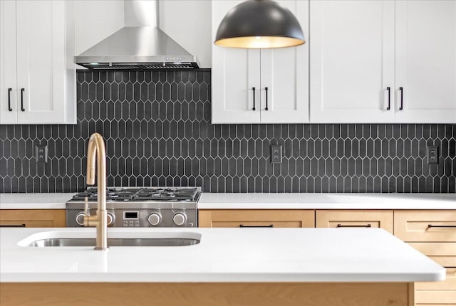kitchen featuring white cabinets, light countertops, a sink, wall chimney exhaust hood, and decorative backsplash