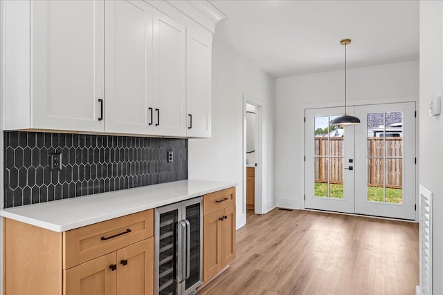 bar with light wood finished floors, wine cooler, baseboards, backsplash, and decorative light fixtures