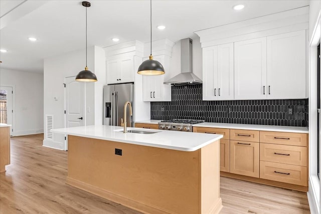 kitchen featuring wall chimney range hood, a sink, light wood-style flooring, backsplash, and appliances with stainless steel finishes