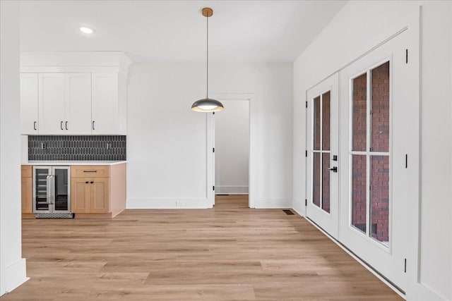 kitchen featuring tasteful backsplash, beverage cooler, hanging light fixtures, and light wood-type flooring