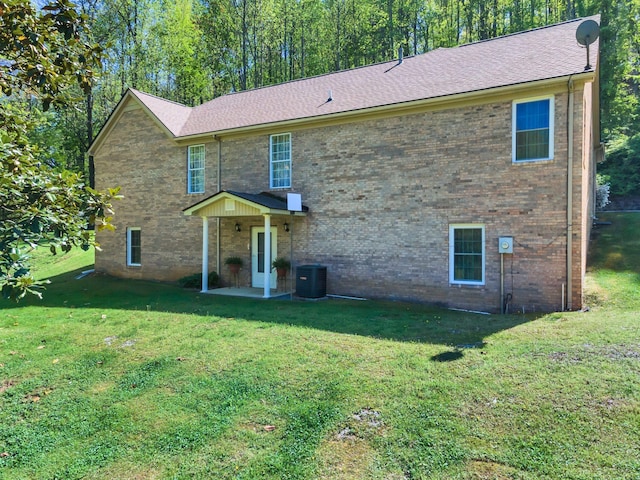 view of front facade with central AC unit, a front lawn, roof with shingles, a patio, and brick siding