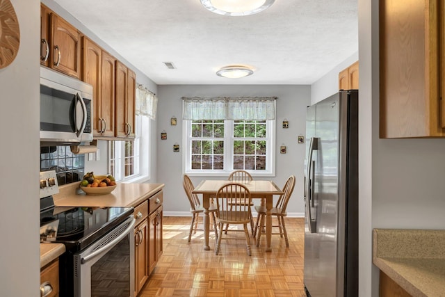kitchen featuring brown cabinets, stainless steel appliances, light countertops, visible vents, and baseboards