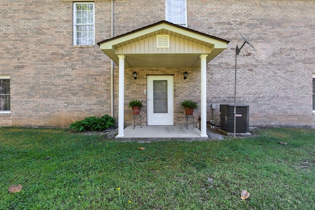 doorway to property featuring central AC unit, brick siding, and a yard