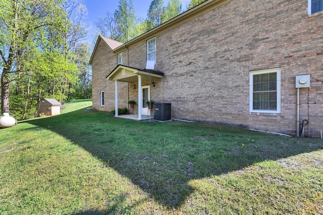back of house featuring a storage unit, brick siding, a yard, and central AC