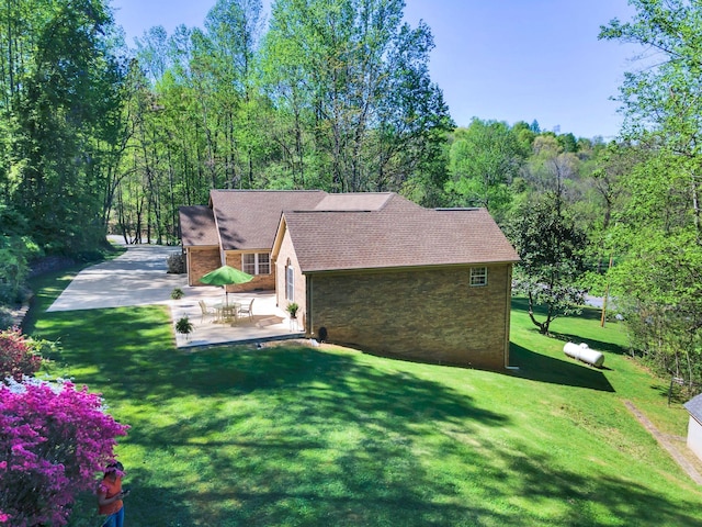view of side of property featuring a patio area, driveway, stone siding, a yard, and roof with shingles