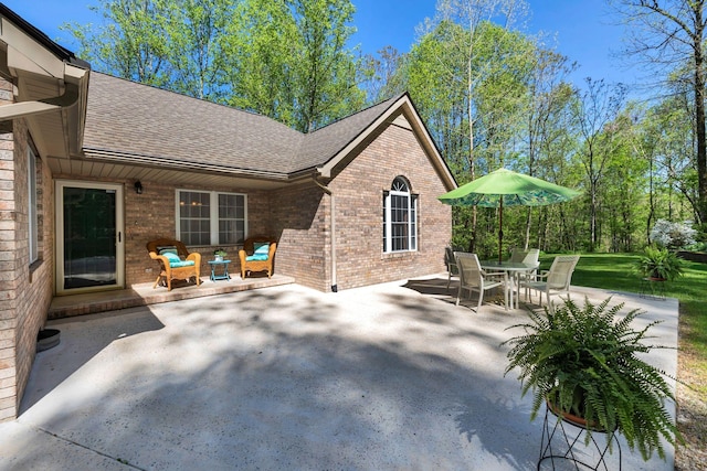 back of house with a patio area, a shingled roof, and brick siding