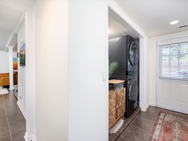 hallway with stacked washer / drying machine, dark tile patterned floors, visible vents, and baseboards