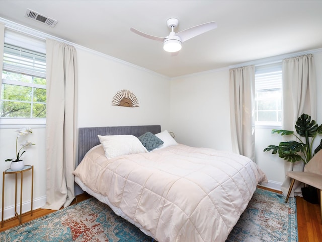 bedroom featuring wood finished floors, visible vents, a ceiling fan, and crown molding