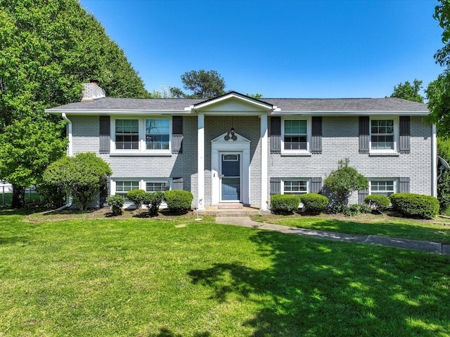 bi-level home with a chimney, brick siding, and a front yard