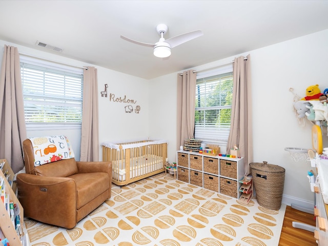 bedroom with a nursery area, baseboards, ceiling fan, and visible vents