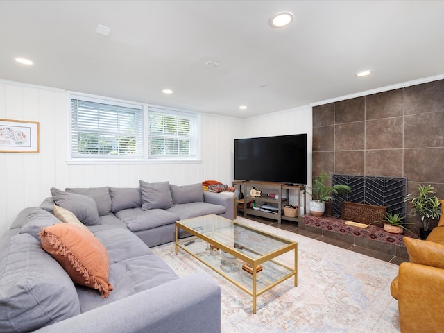 living area with a tile fireplace, recessed lighting, and ornamental molding