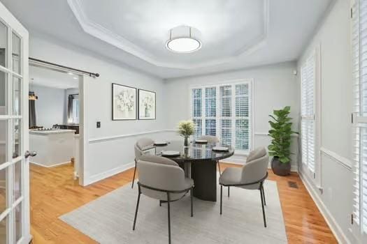 dining room featuring a tray ceiling, light wood-style floors, and french doors