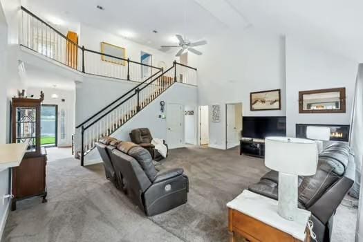 carpeted living room with a towering ceiling, stairway, and a ceiling fan
