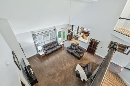 carpeted living area with a ceiling fan, a high ceiling, and baseboards