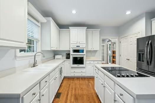 kitchen with black appliances, a sink, a center island, light countertops, and white cabinetry