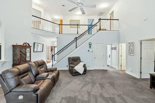 carpeted living room with a towering ceiling, ceiling fan, stairway, and baseboards