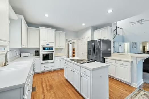 kitchen featuring black appliances, a center island, light countertops, white cabinetry, and recessed lighting