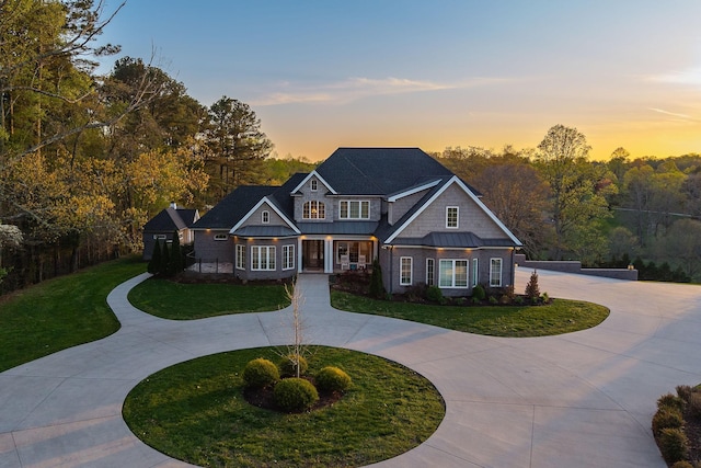 view of front of home featuring covered porch, curved driveway, a yard, metal roof, and a standing seam roof