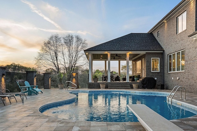 pool at dusk with grilling area, fence, a patio, and a fenced in pool